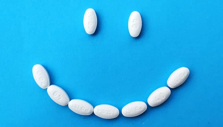 White pills arranged to make a smiley face on a blue background