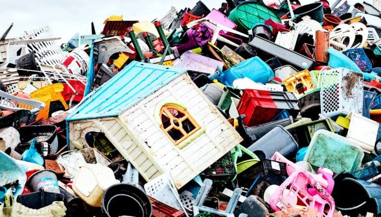 A landfill pile hold all sorts of plastic items from lawn chairs to containers, but most prominent is a child's playhouse sitting in the mess