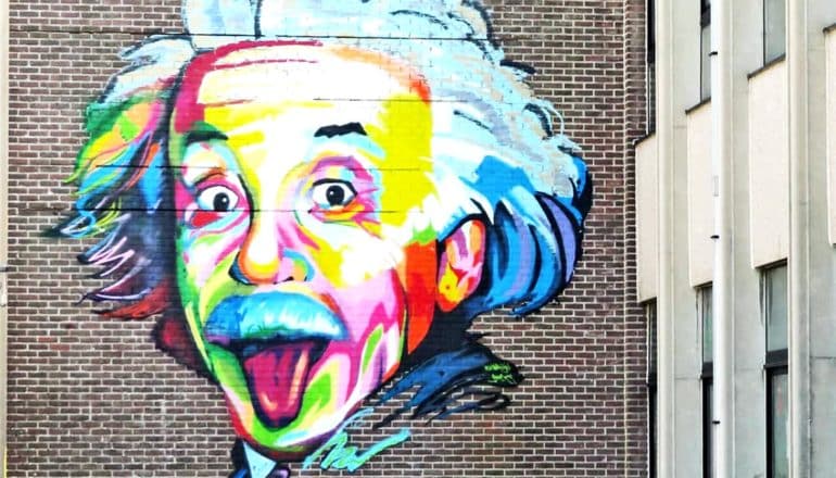 A colorful painting of Einstein sticking his tongue out on a dark brick building