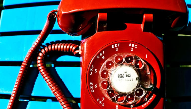 A red retro dial phone sits on a blue table