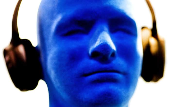 A blue mannequin head has headphones on against a white background