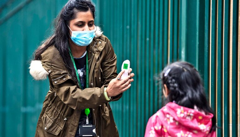 A woman shows a child her temperature on a thermometer as they both wear masks