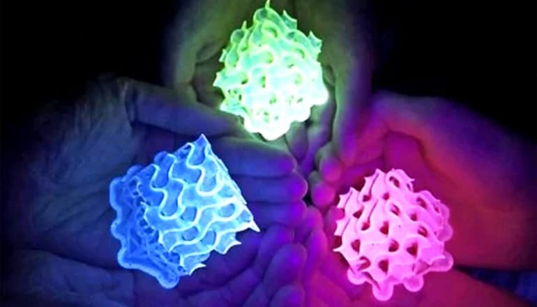 Hands hold 3 different colored SMILES fluorescent materials, one glowing green, one blue, and one pink