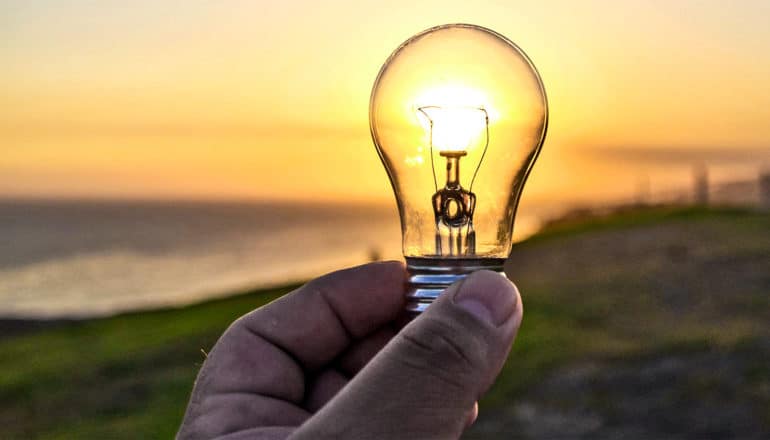 A person holds up a lightbulb so that sunlight shines through