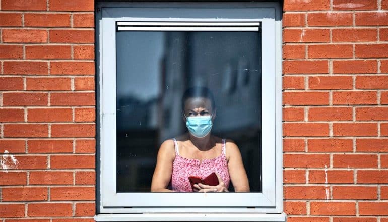 A woman in a mask looks out a window