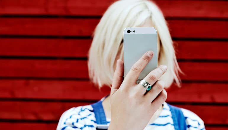 A woman holds an iPhone in front of her face while standing in front of a red wall