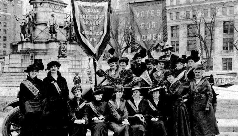 Women pose for a picture holding banners advocating for women's suffrage