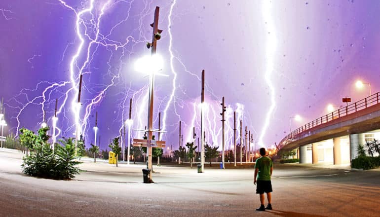 A man looks up from a parking lot to see a purple sky filled with white lightning