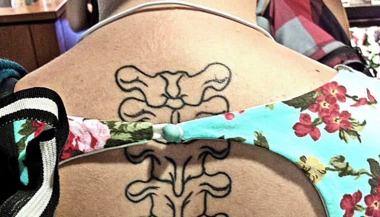 A young person has a spine tattoo on their back