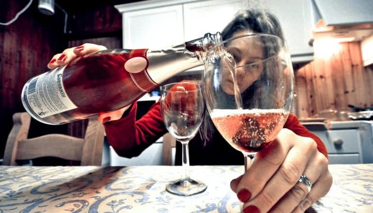 A woman pours wine into a glass she's looking through