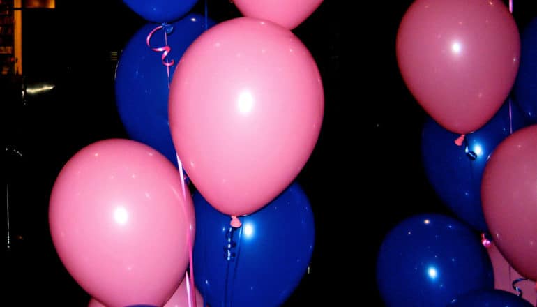 Pink and blue balloons float in a dark room