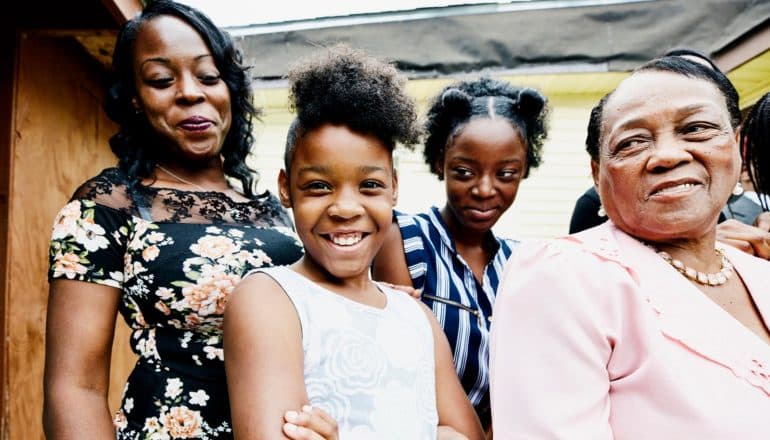 four dressed-up Black women; three adults look proudly at teen