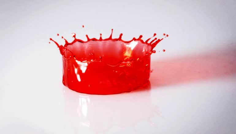 A drop of red liquid splashes on a gray surface