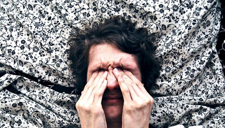 A man rubs his eyes while his head rests on a flowery pillow