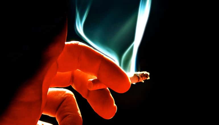 A person's hand holds a lit cigarette