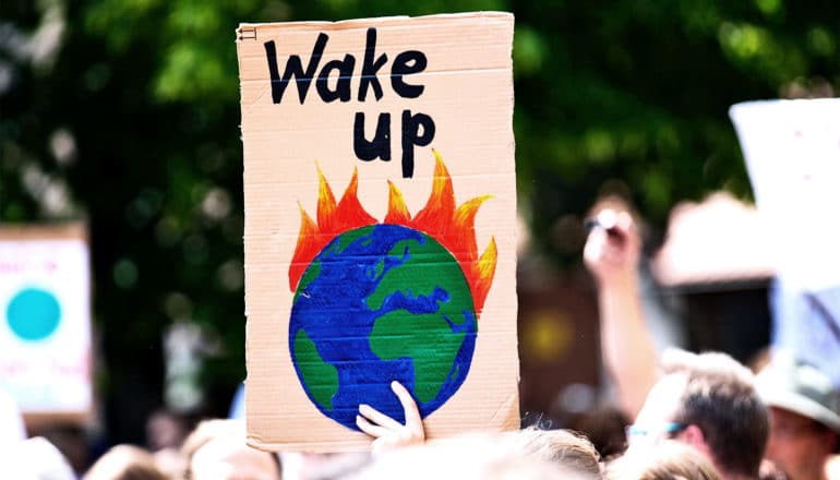 A person at a protest for climate change action holds a sign with an image of Earth on fire that reads, "Wake Up"