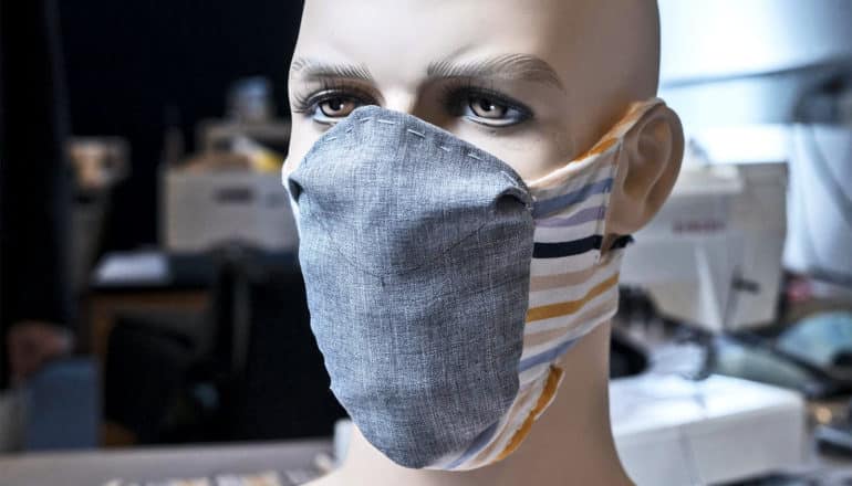 The prototype face mask on a mannequin head. The mask has a gray fabric front section and multi-colored bands of fabric around the back of the head and under the chin