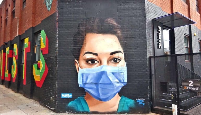 A mural shows a doctor with a blue face mask painted on a brick wall