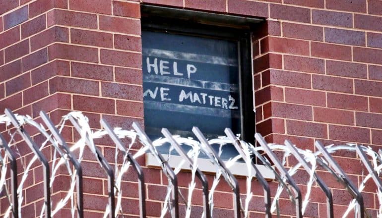 "help we matter 2" on window behind razor wire