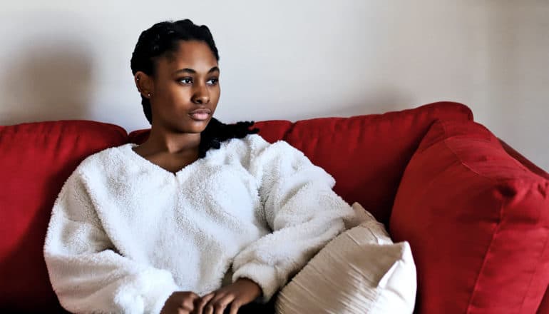 A young woman looks lost in thought while sitting on a red couch