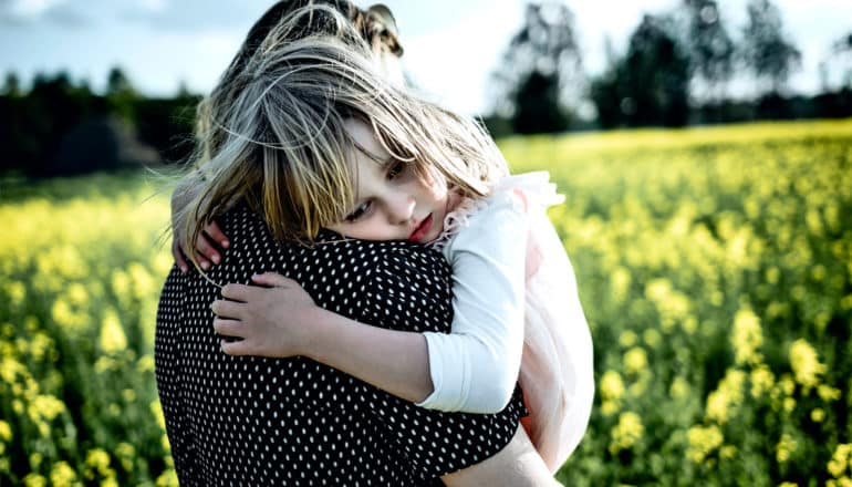 A mother holds her daughter, who leans on her shoulder