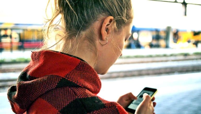 A young woman looks down at a phone while standing outside