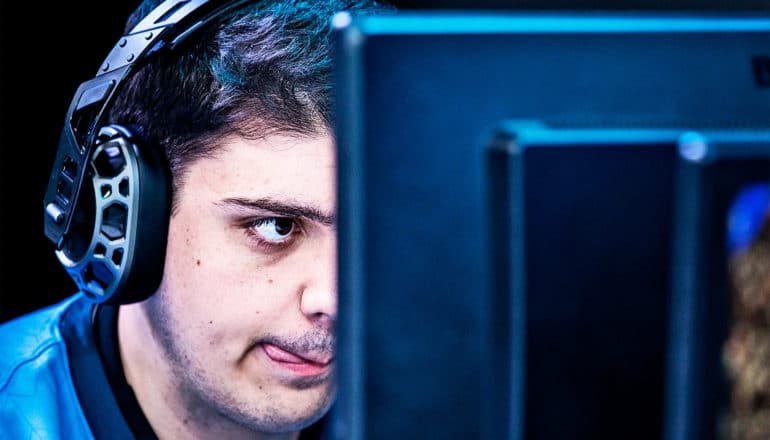 A young man stares at a computer screen with his tongue sticking out in concentration