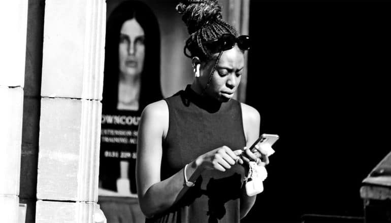 A young woman walks down the street looking down at her phone with a concerned or confused look