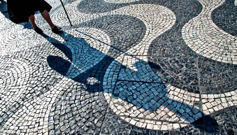 An older woman walks over a stone walkway with a wavy pattern