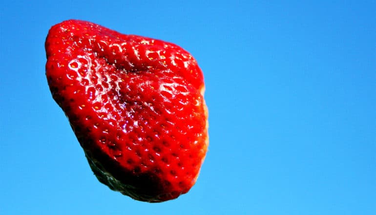 A strawberry sails through blue sky