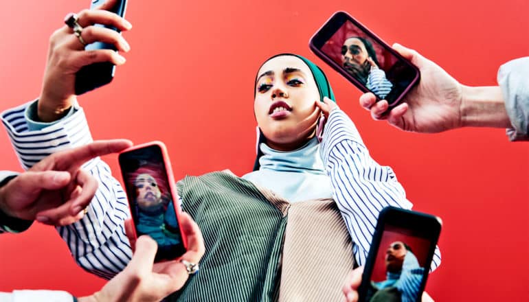 A woman snapping a selfie is surrounded by other people holding phones to take her picture