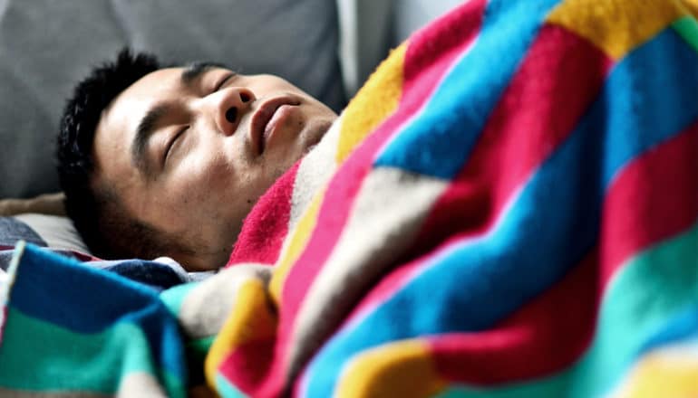 A man sleeps on a couch under a colorful blanket