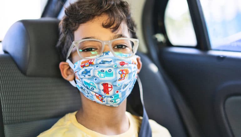 child wears colorful mask in car