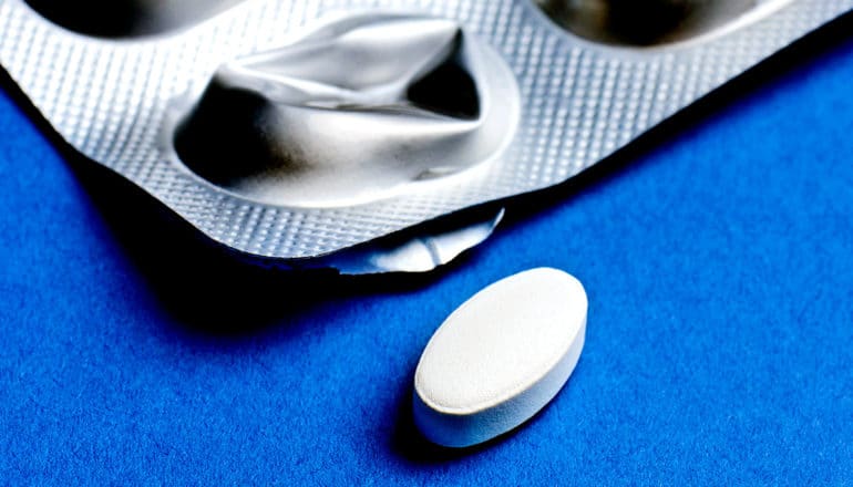 A pill and blister pack sit on a blue background