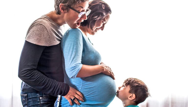 kid kisses pregnant belly of one of two moms