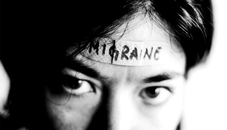 A young woman has a band-aid on her forehead with the word "Migraine" on it in pen