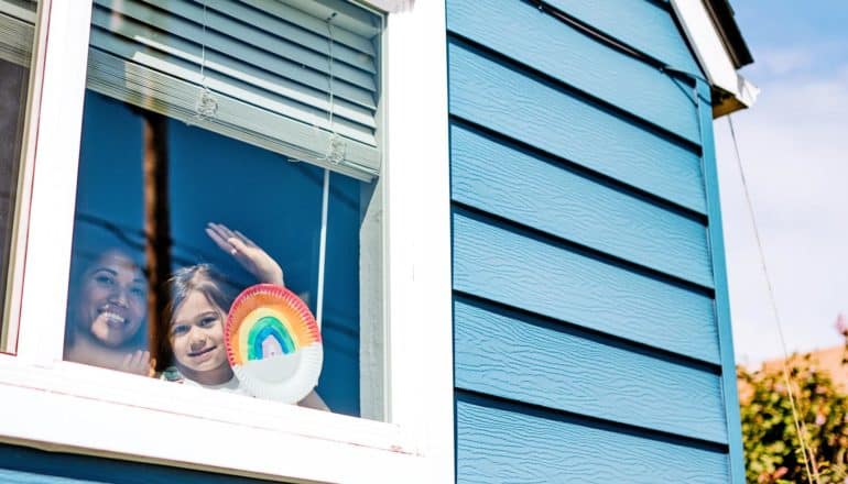 adult and child wave from window with rainbow decoration