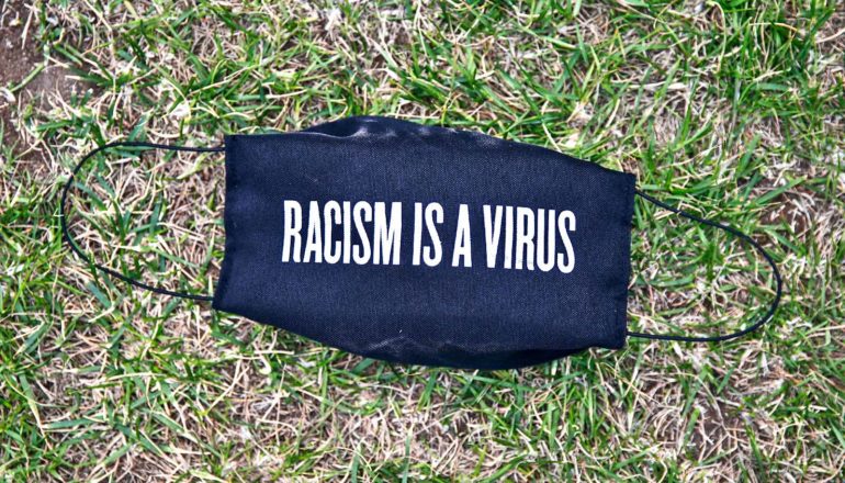 A black face mask on grass reads "Racism is a virus."