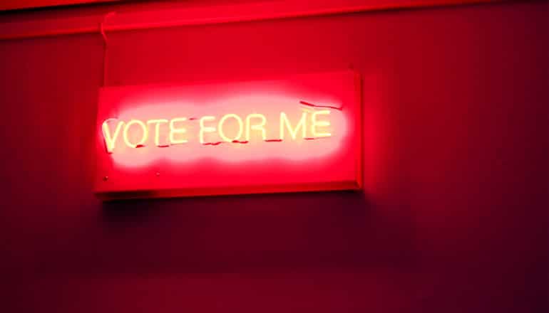 A red neon sign with yellow letters reads "Vote for Me"