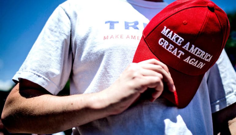 A person holds a red Make America Great Again hat over their heart