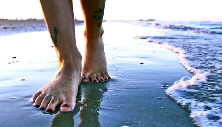 A person walks barefoot on the beach right next to the ocean