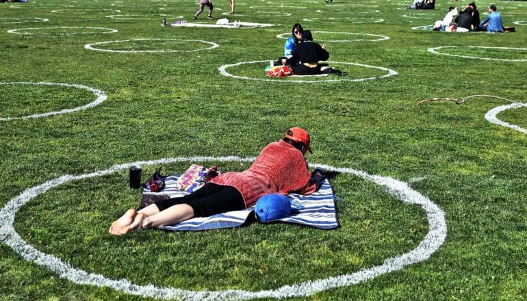 People sit in white circles painted on grass at a park