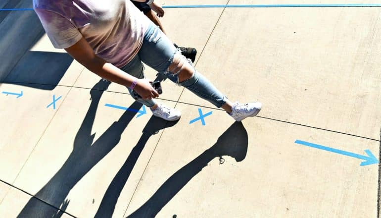 Two people walk on concrete with blue tape on it to indicate six feet of social distance