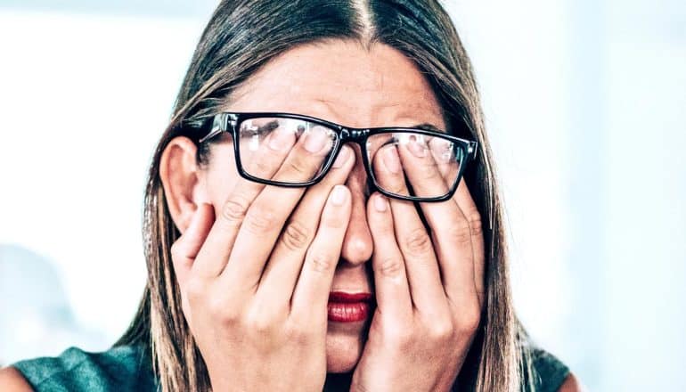 A woman rubs her eyes, putting her hands under her glasses