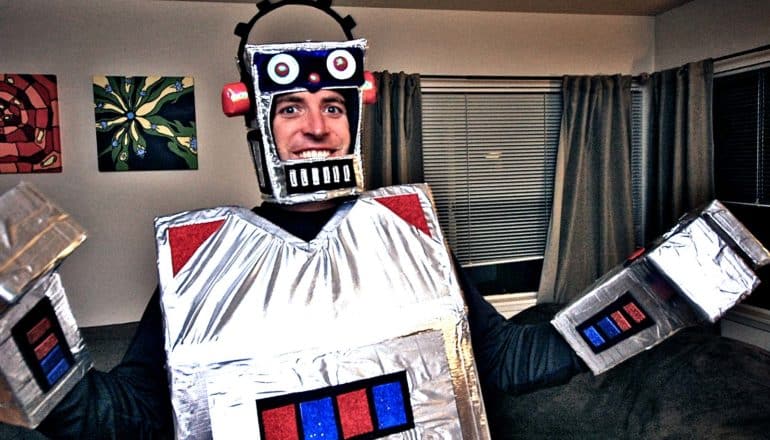 A man wears a robot costume made from cardboard boxes in his living room