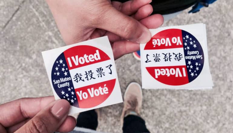 hands hold stickers that say "I Voted!" San Mateo county in English, Spanish, and Chinese