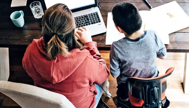 A mother and son sit at a table looking at a laptop