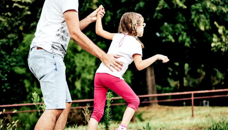 A dad helps his daughter with cerebral palsy walk through the woods