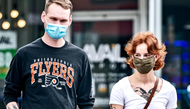 A man and woman in face masks walk across a city street