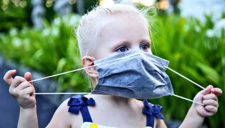 A little girl pulls at her fabric mask